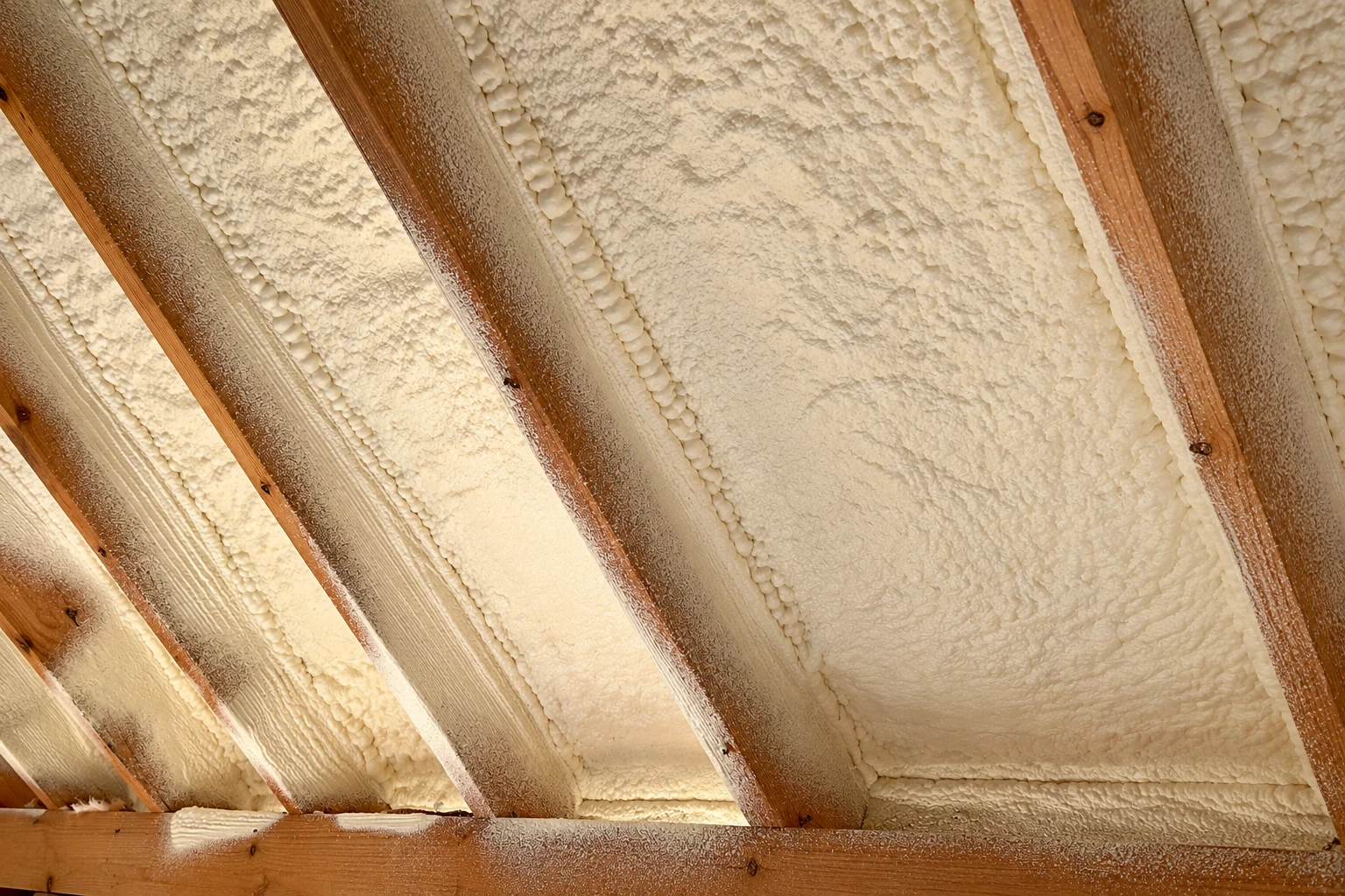 Open-cell spray foam fills the spaces between exposed wooden roof rafters.