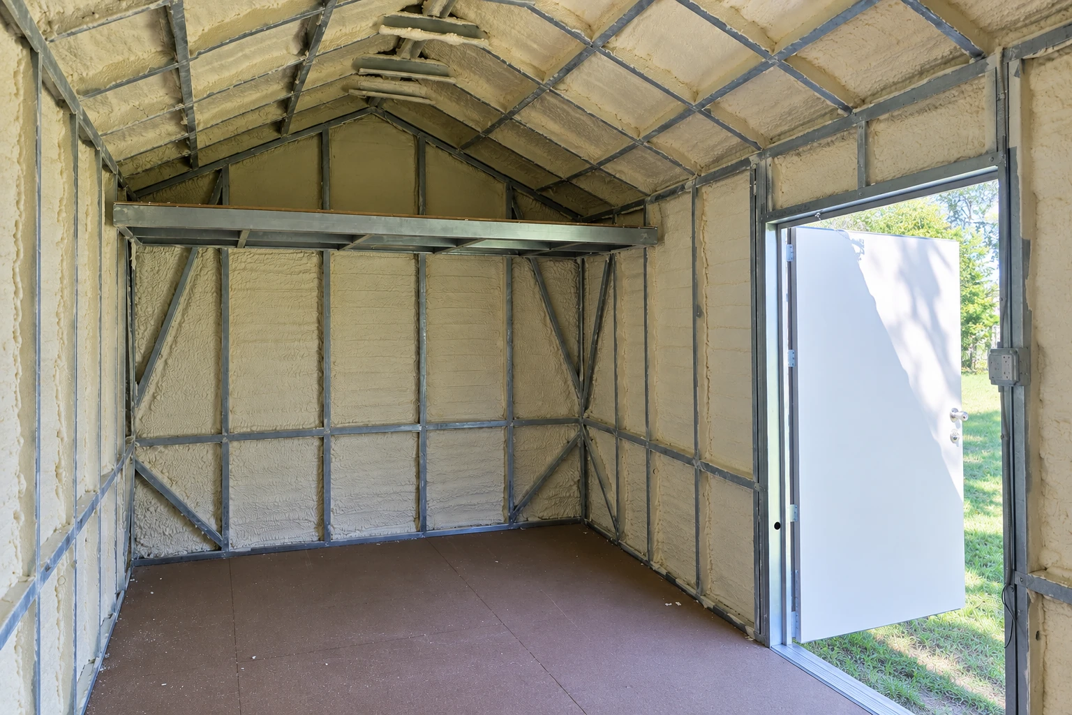 A small metal-framed building is lined with pale spray foam insulation across its walls and sloped ceiling.